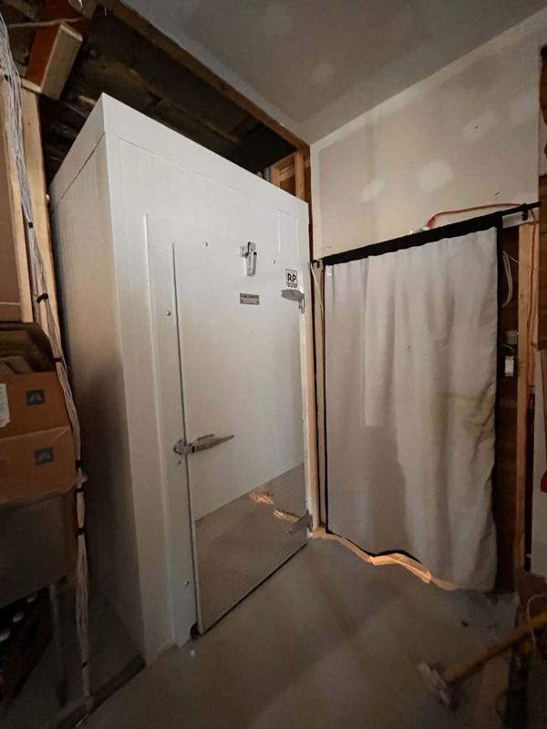 Petite chambre froide blanche avec porte à plaque de protection, installée dans un sous-sol